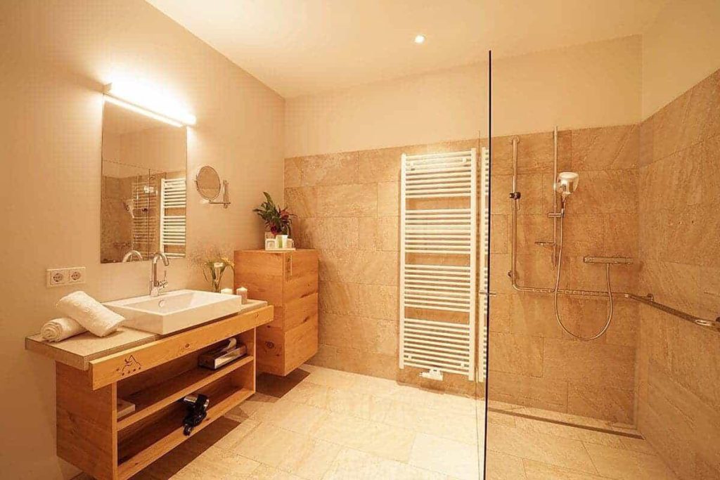 Moderne Badezimmerausstattung mit Holzbadmöbeln und großer Dusche in den Adler Alpen Apartments.
