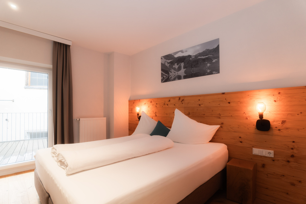 Modernes Schlafzimmer mit Doppelbett, Holz-Kopfteil und Balkonzugang in den Adler Alpen Apartments